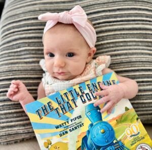 Elizabeth Newbould's daughter poses with a Dolly Parton Imagination Library book, the Little Engine Who Could.