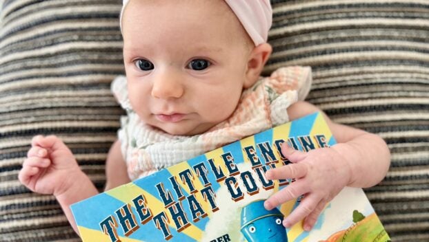 Elizabeth Newbould's daughter poses with a Dolly Parton Imagination Library book, the Little Engine Who Could.